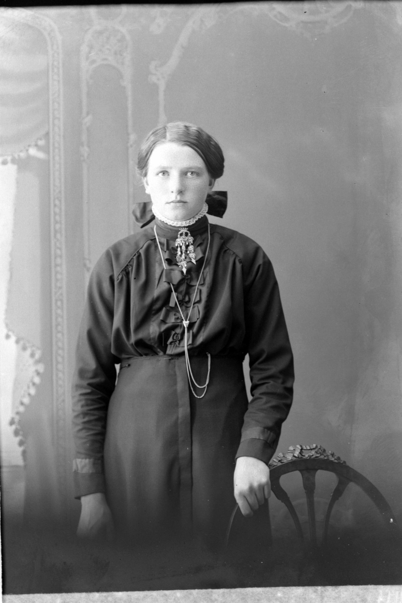 Studioportrett av en kvinne med hånden på en stolrygg.