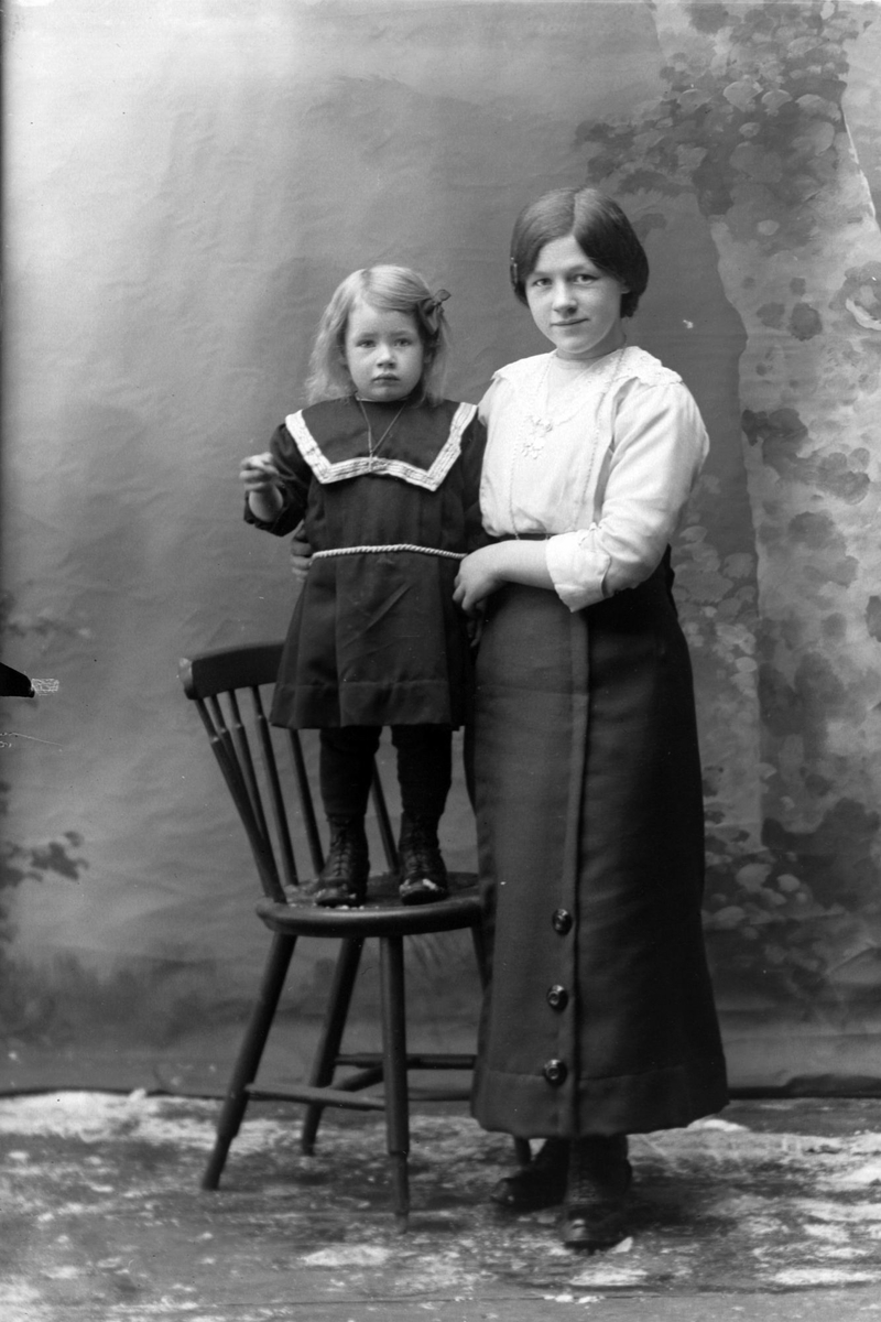 Studioportrett av en kvinne med et barn ved siden av seg.