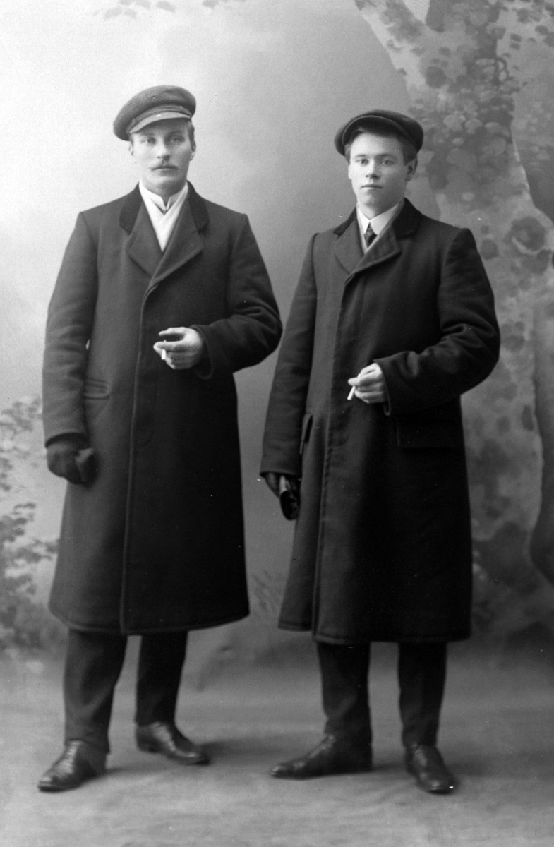 Studioportrett av to menn med frakker og luer.