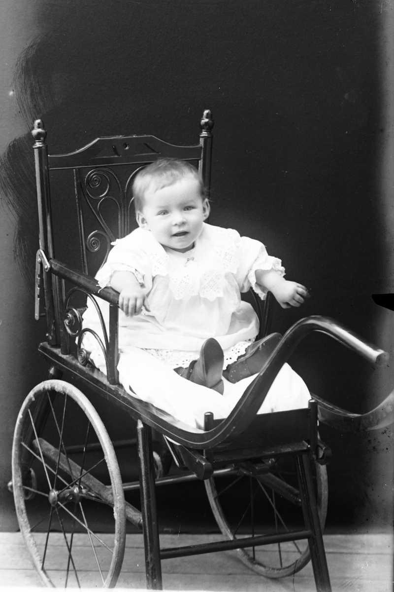 Studioportrett av et lite barn sittende på en vogn.