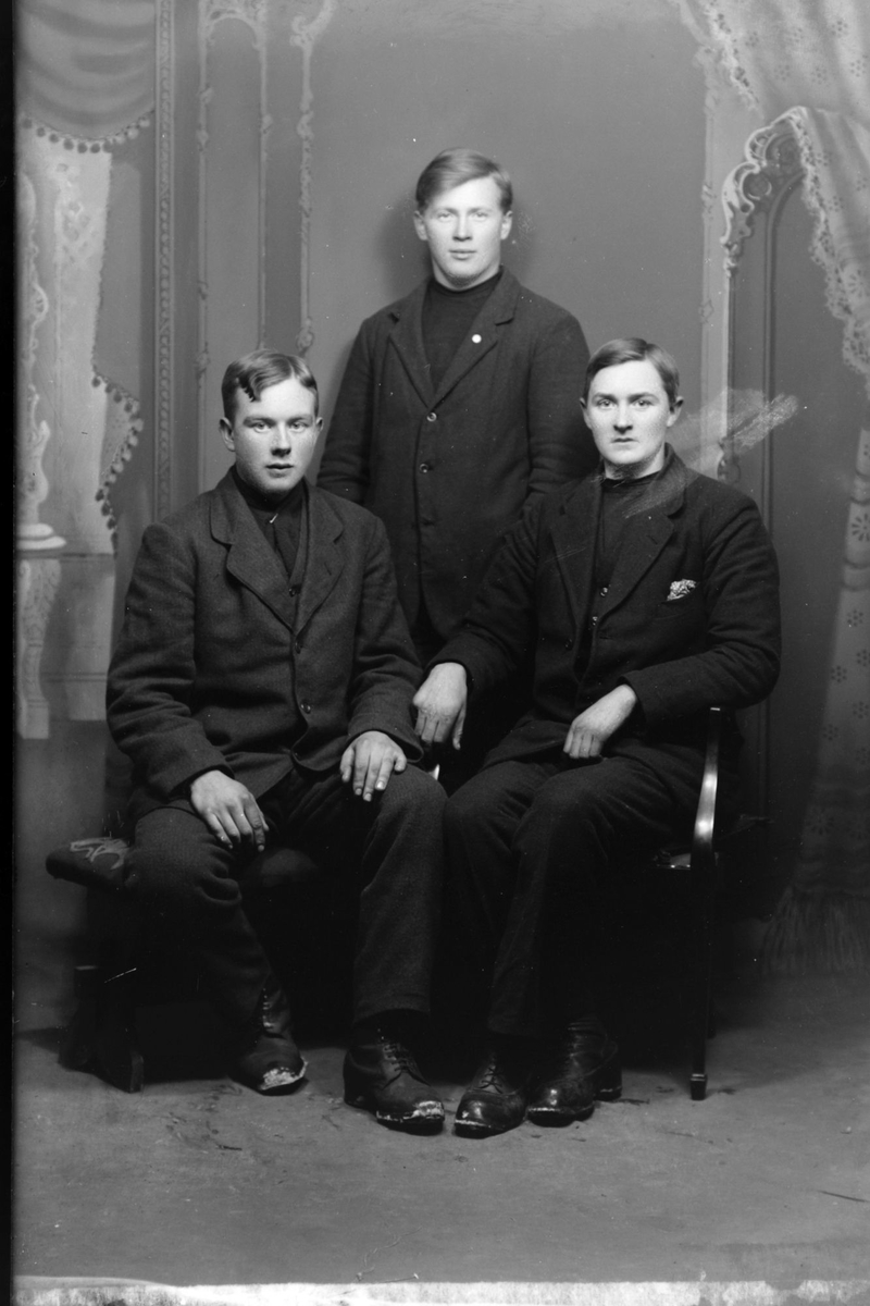 Studioportrett av tre menn i mørke klær.