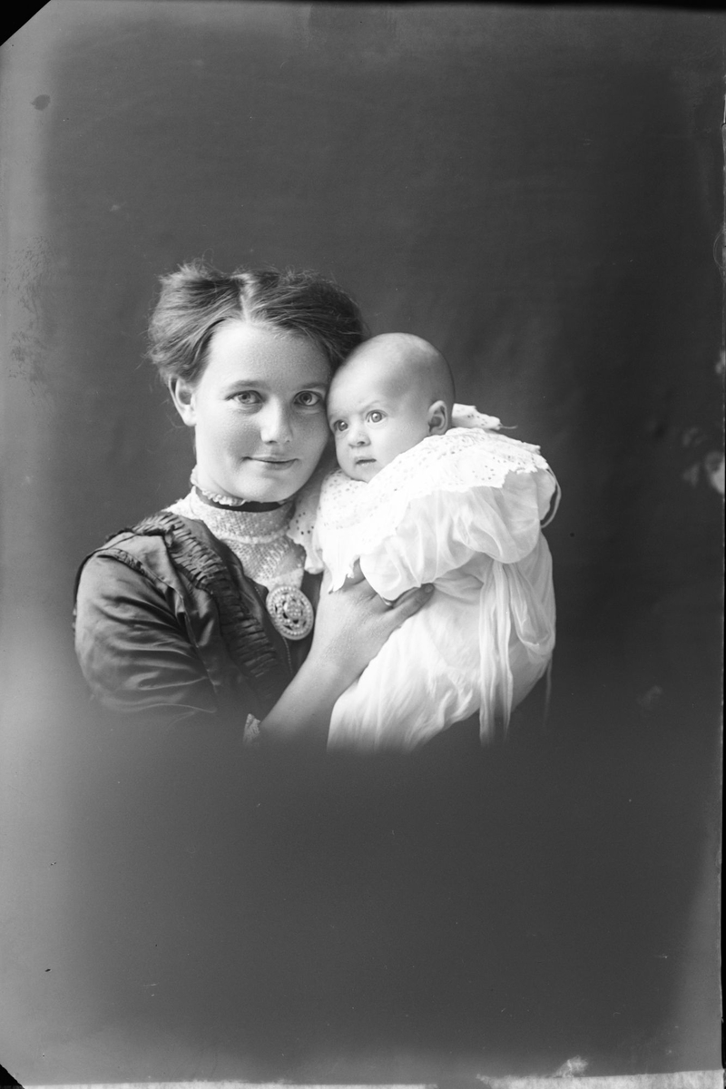 Studioportrett av en kvinne med et spedbarn i armene.