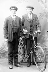 Studioportrett av to menn med en sykkel.
