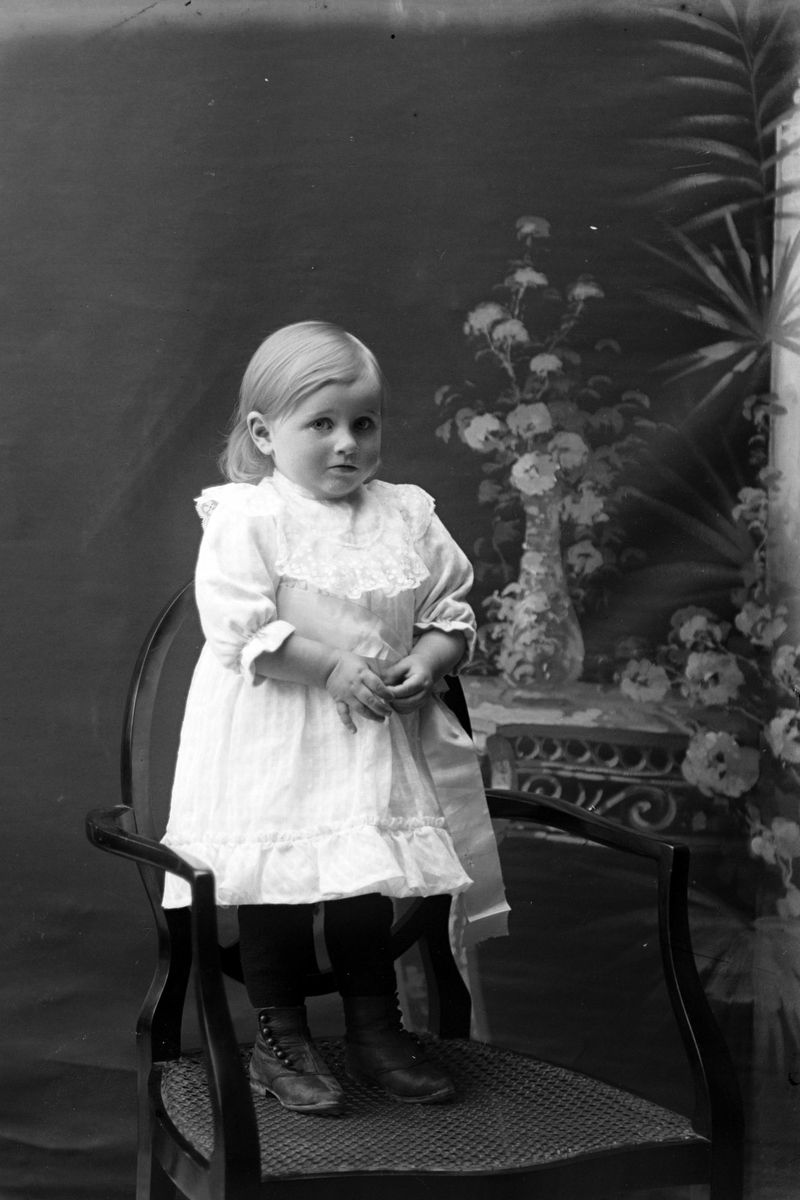 Studioportrett av en liten jente kledd i en hvit kjole.