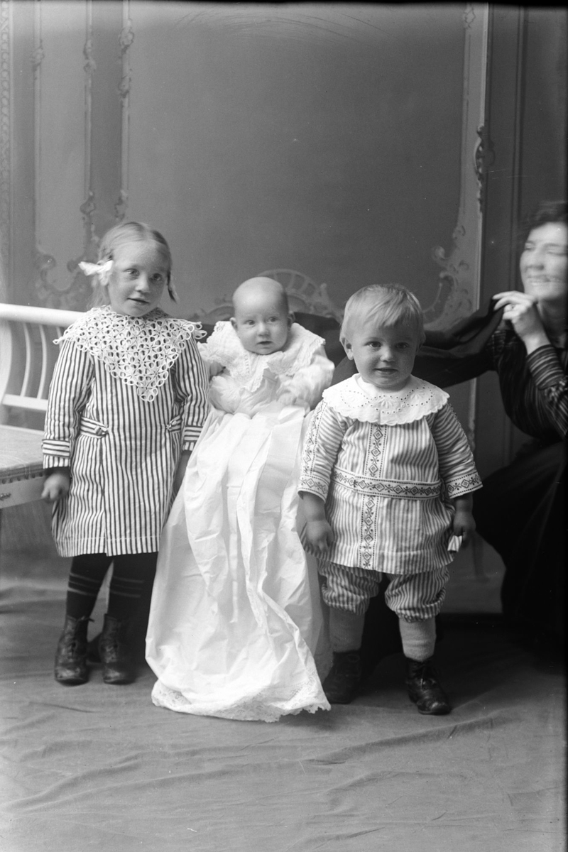 Studioportrett av tre barn ved siden av en kvinne.