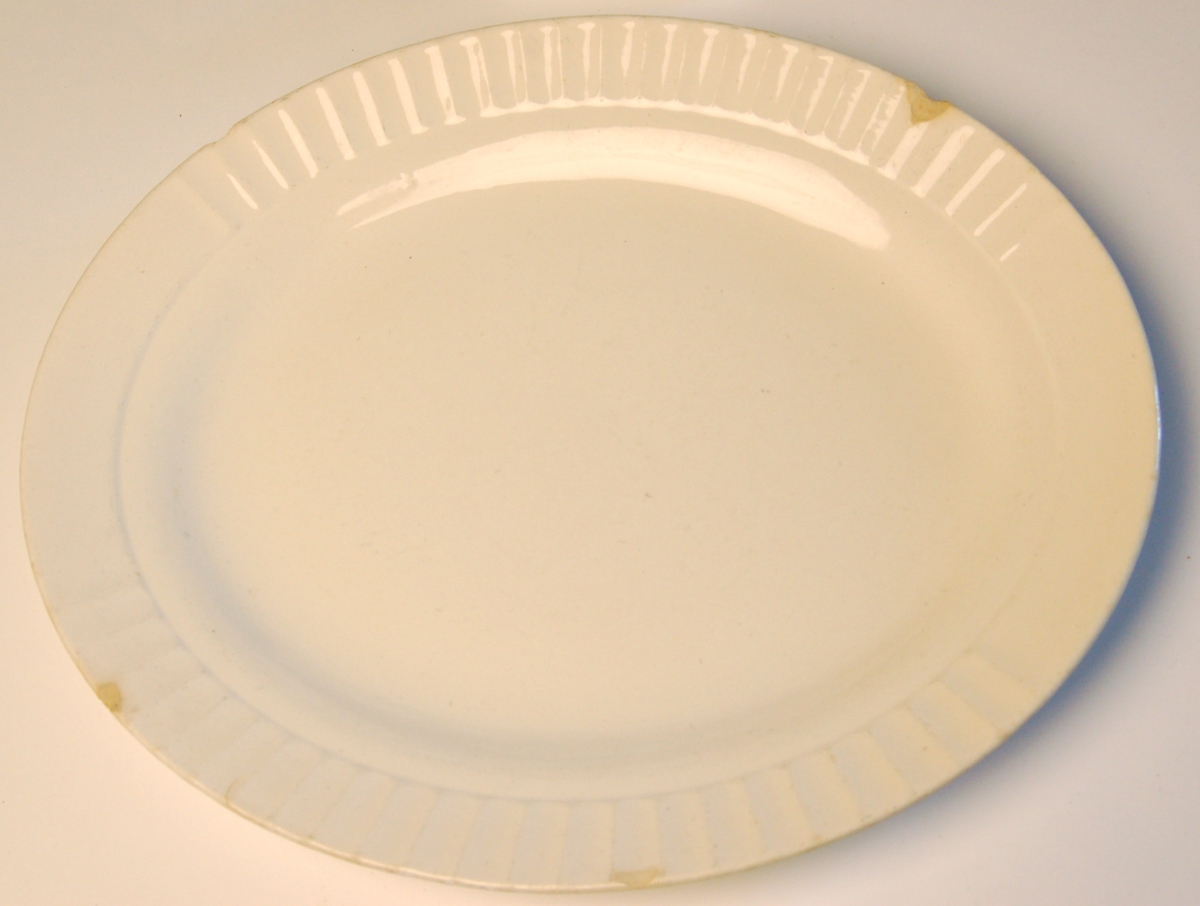 Ovalt porselen serveringsfat med bølgedekor rundt ytterkant av fatet.