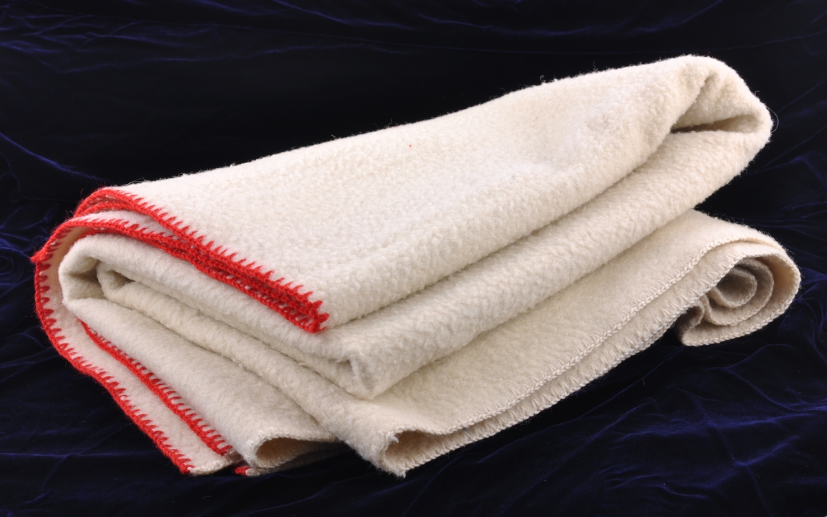 Ullteppe, vevd og tovet. Tre deler er sydd sammen til et teppe.Heklekant med rød og hvit ullgarn.