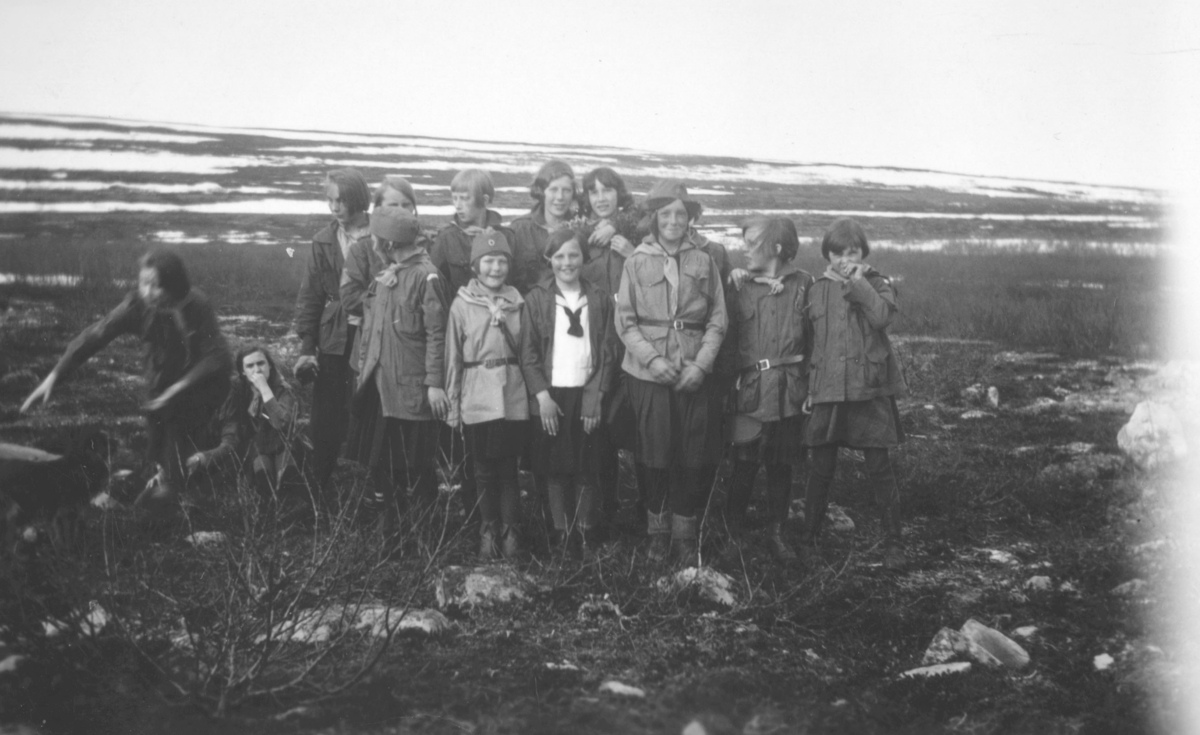 Bildet er tatt i Tomaselv våren 1933, ovenfor Hoels hytte. En gruppe speiderjenter er på tur. De er kledt i uniformer. I området er det kratt. Fjellet ses i bakgrunnen. Det ligger snø der. Bak fra venstre står Ella Gunnari, Vera Hoel, ukjent jente, Ingeborg Haave, og Dagny Nordahl. Foran fra venstre Brit Hornburg, Arnhild Tøgersen, tre jenter med Saxi som etternavn, Borghild Dahl, og en jente med etternavn Pedersen