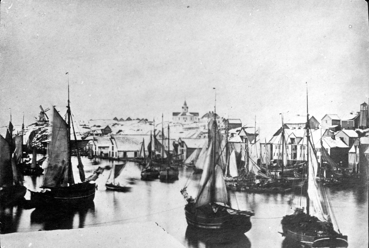 Parti av Haugesund havn, sett fra nordpynten av Risøy 1865. Til høyre for kirken vil en gjenkjenne O. M. Christensens hus. ytterst til høyre arbeids- og brannklokken på Tuhaug, oppsatt 1863.