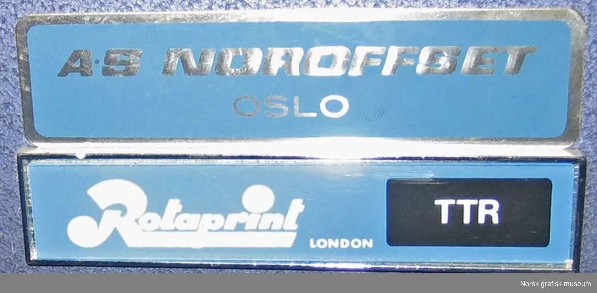 Liten offsetpresse med blålakkert metalldeksel. Har et plastovertrekk med Rotaprint-logo.