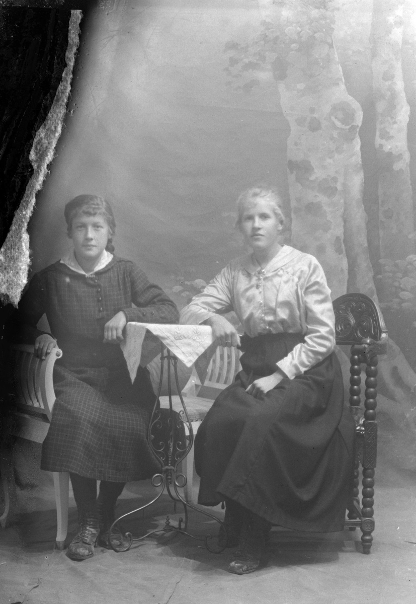 Studioportrett av to kvinner sittende ved et bord.