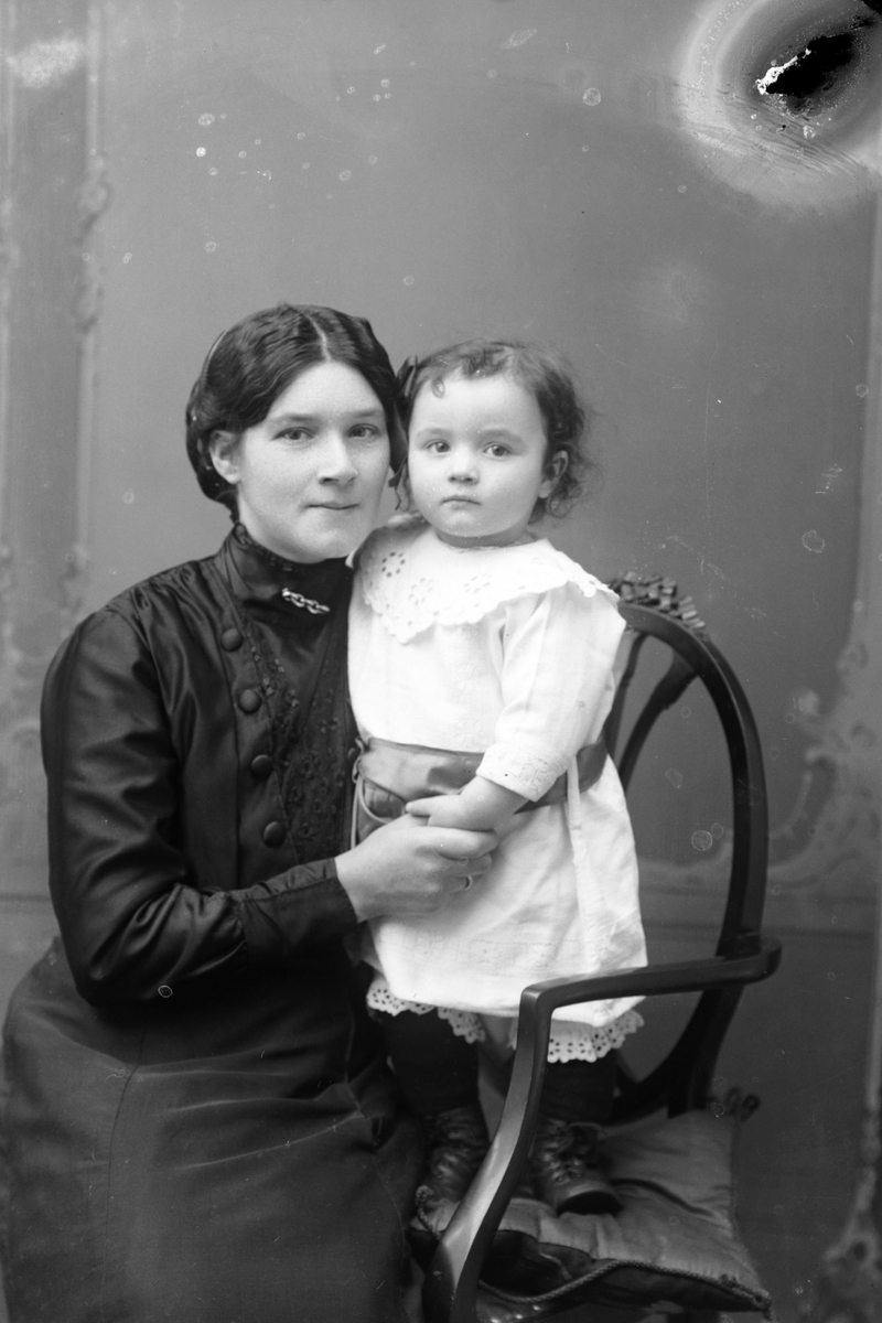 Studioportrett av en kvinne med et barn i armene.