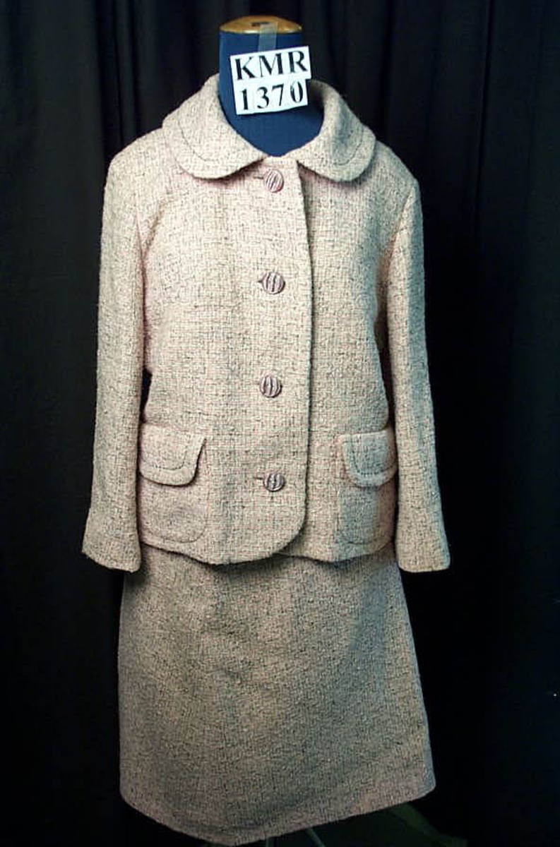 Drakt, skjørt og jakke, store lillarosa farget knapper i fronten på jakken. liten krage. Både jakke og skjørt er helforet med grått nylonfor. 