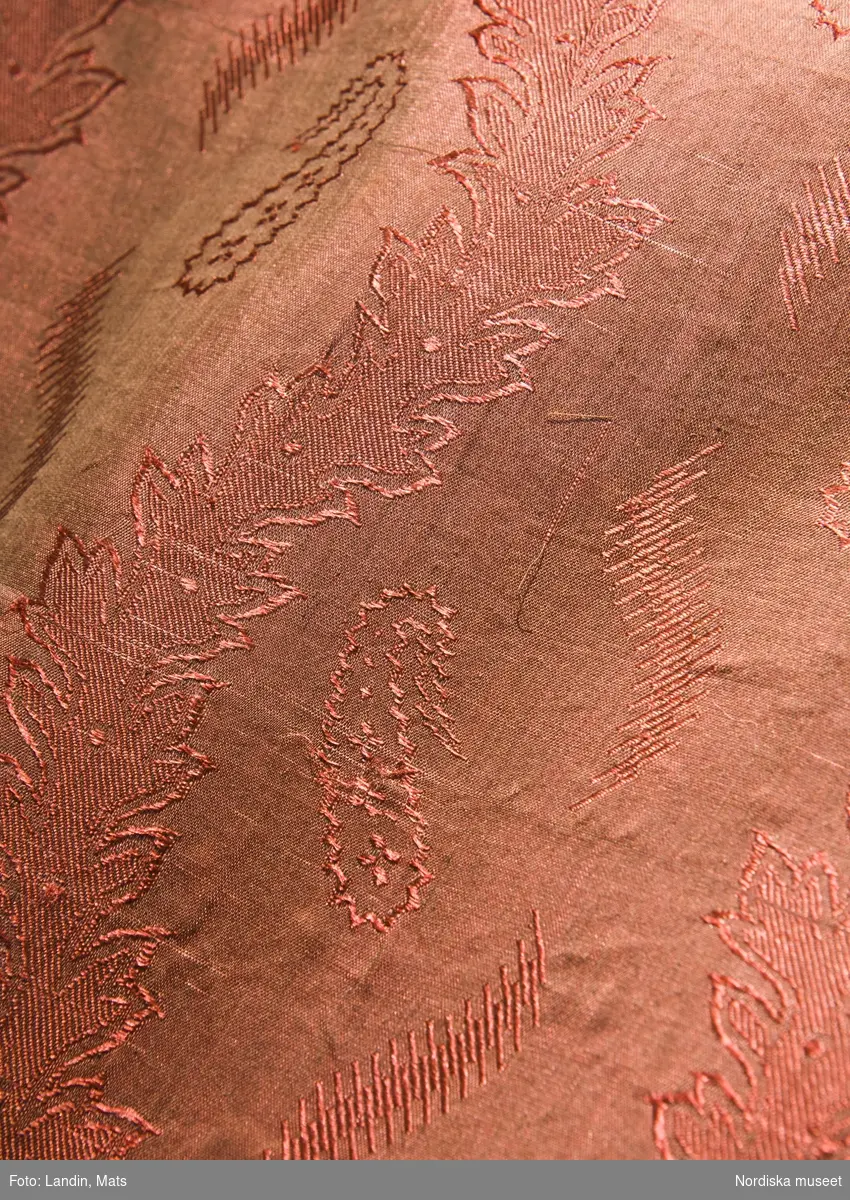 Lönklänning, kvinnlig dräkt, Rådmansö (Uppland)

, omkring 1850. 
Halvylle.
Av hemvävt smalrandigt halvylle. Varpen är av ljusbrunt bomullsgarn, inslaget i tuskaft av svart tunt ullgarn med smala ränder i ullgarn samt smala streckränder i gult och vitt silke. Figursytt liv med ränderna diagonalt och med sneda insyningar. Lång ärm på diagonalen,  med två smala sammetsband nedtill.  Veckad kjol i ett stycke, mitt bak tätare veckning. Livet och ärmarna är  fodrade med vit bomullslärft. Modellen är påverkad av 1850-talets modedräkt. Vävd och sydd av Kristina Lindström f. 1830, av garn hon fått som lön när hon arbetade som piga.

Förkläde, kvinnlig dräkt, Munktorp i Västmanland, 1800-talets mitt. Halvsiden.
Av tunt mönstrat halvsiden. Varpen är av fint ljusbrunt bomullsgarn, inslaget av orangerött silke. Botten i tuskaft med jacquardvävt mönster med bladslingor och mellan dessa små mir-i-botafigurer och streckfigurer. Tyget är bara 50 cm brett och har därför sytts ihop på mitten.  I midjan lagda veck, fastsydda knytband av bruna bomullsband. Halvsidentyger kom på modet i folklig dräkt vid 1800-talets mitt som en ersättning för de dyrbarare äkta sidentygerna. Vanligt även i livstycken och västar. Miribota, indisk benämning på det vanligaste mönstret i "äkta" schalar. Brukar nu kallas ”paisleymönster”.

Halskläde, kvinnlig dräkt, Alsike (Uppland), sidenväveri, Stockholm, 1847. Siden.
Halskläde av siden, mönstervävt troligen med jacquardvävstol. Svart varp. Inslaget i rödrosa, ljusviolett, gult, grönt och vitt ligger sektionsvis i bårder, vilket inte syns i framsidans mönster. Inknutna långa silkefransar av mönstrets färger. I ena hörnet finns en svart rund stämpel med texten: "Stockh. Hallstemp. 1847". Sidenduken var en vanlig gåva från fästmannen till den blivande bruden, köptes oftast på någon marknad.

Bindmössa, kvinnlig dräkt, Frötuna (Uppland), tillhört och burits av Greta Persdotter (1809-1877). Sidensatin.
Bindmössa av vit sidensatin med enfärgat tambursömsbroderi i orange. Sex veck vid vardera sidan, dragband i nacken av vitt linne, fodrad med gul bomullslärft (domestik). Nackrosett  av 5,5 cm brett sideband med blommönster i orange på vit botten, avpassat efter mössans färger.