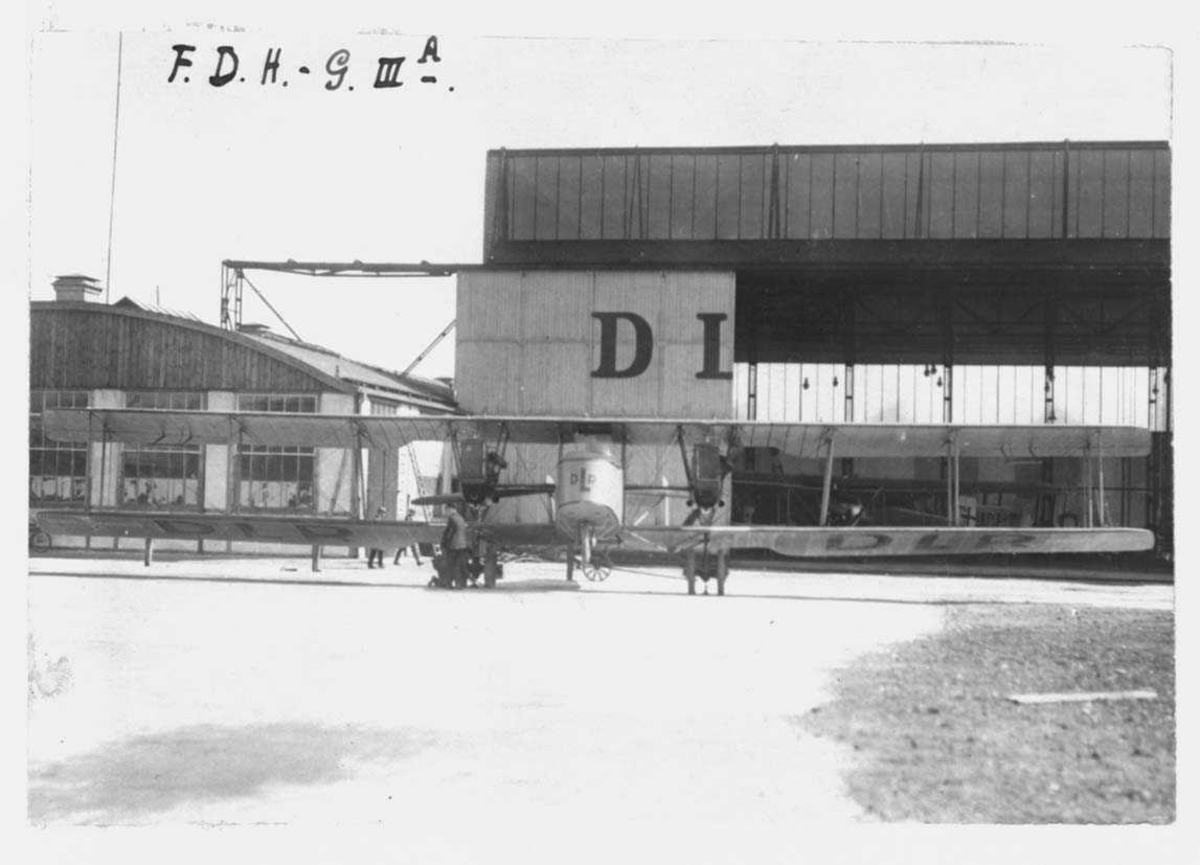 Ett fly på bakken. Friedrichshafen 45 (G.IIIa) of Deutsche Luftreederei (DLR). Hangarer i bakgrunn