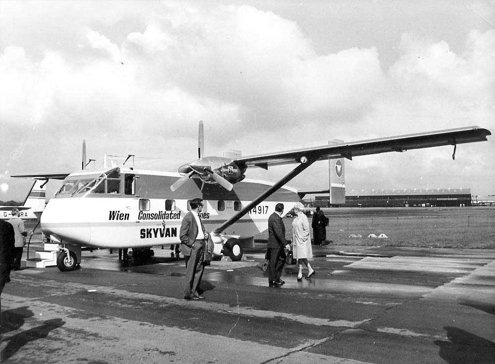 Lufthavn. Ett fly på bakken, Shorts Skyvan Srs 3 N4917 fra Wien Consolidated Airlines. Flere personer ved flyet. Bygning i bakgrunnen.