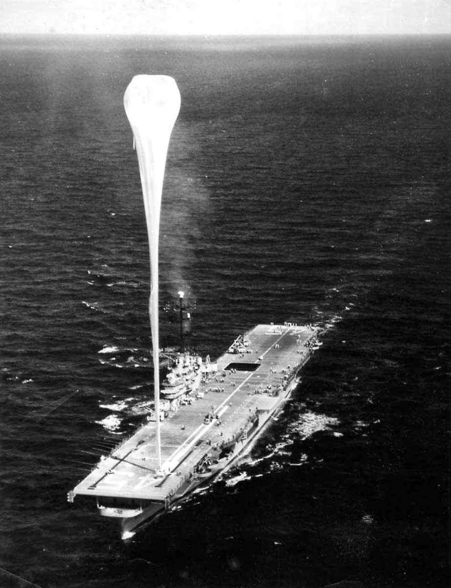 Ett hangarskip i sakte fart på vannet, USS Valley Forge. En ballong som er festet på dekket til hangarskipet, går høyt opp i luften.