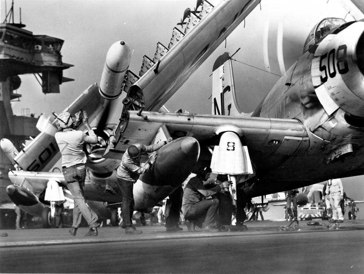 Ett fly på dekket til et hangarskip, Dogulas Skyraider AD-4 med vingene oppslått, som blir plassert på en katapult. Flere personer som klargjør flyet.