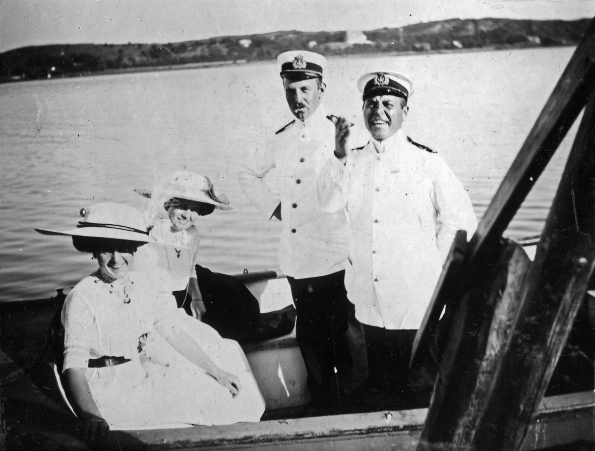 Sällskap poserar glatt i mindre båt iklädd uniform och långklänning. Kapten Gisiko och Jacobi med frökrarna Sjöholm under party på Blenda.