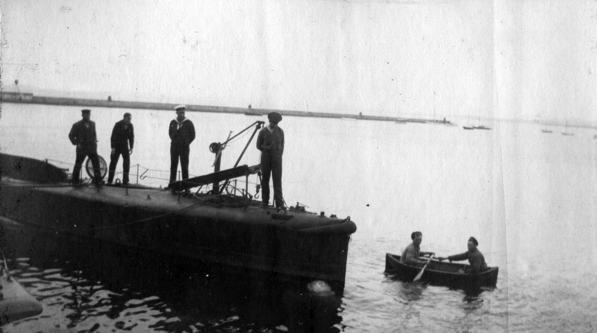 Marstrand  1916-1917. Fyra sjömän står på ubåtsdäck och kollar ner i vattnet där en jolle glider förbi med två personer i.