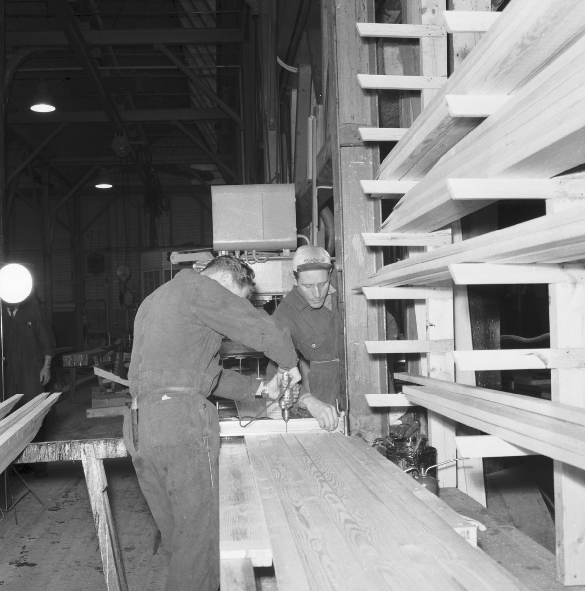 Bilden visar två varvsarbetare som bearbetar spant för träminsveparen M 60 med en borrmaskin.
