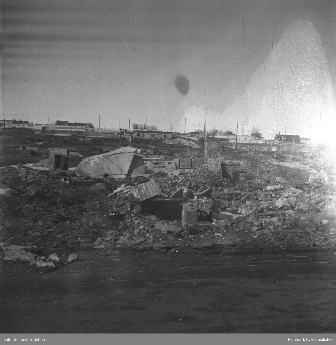 Ruiner av et hus i Vadsø 1946, trolig Godtfred Johansens bakeri.  På bildet ser vi bare det som er igjen av grunnmuren. Lengre bak på bildet brakkebyen.