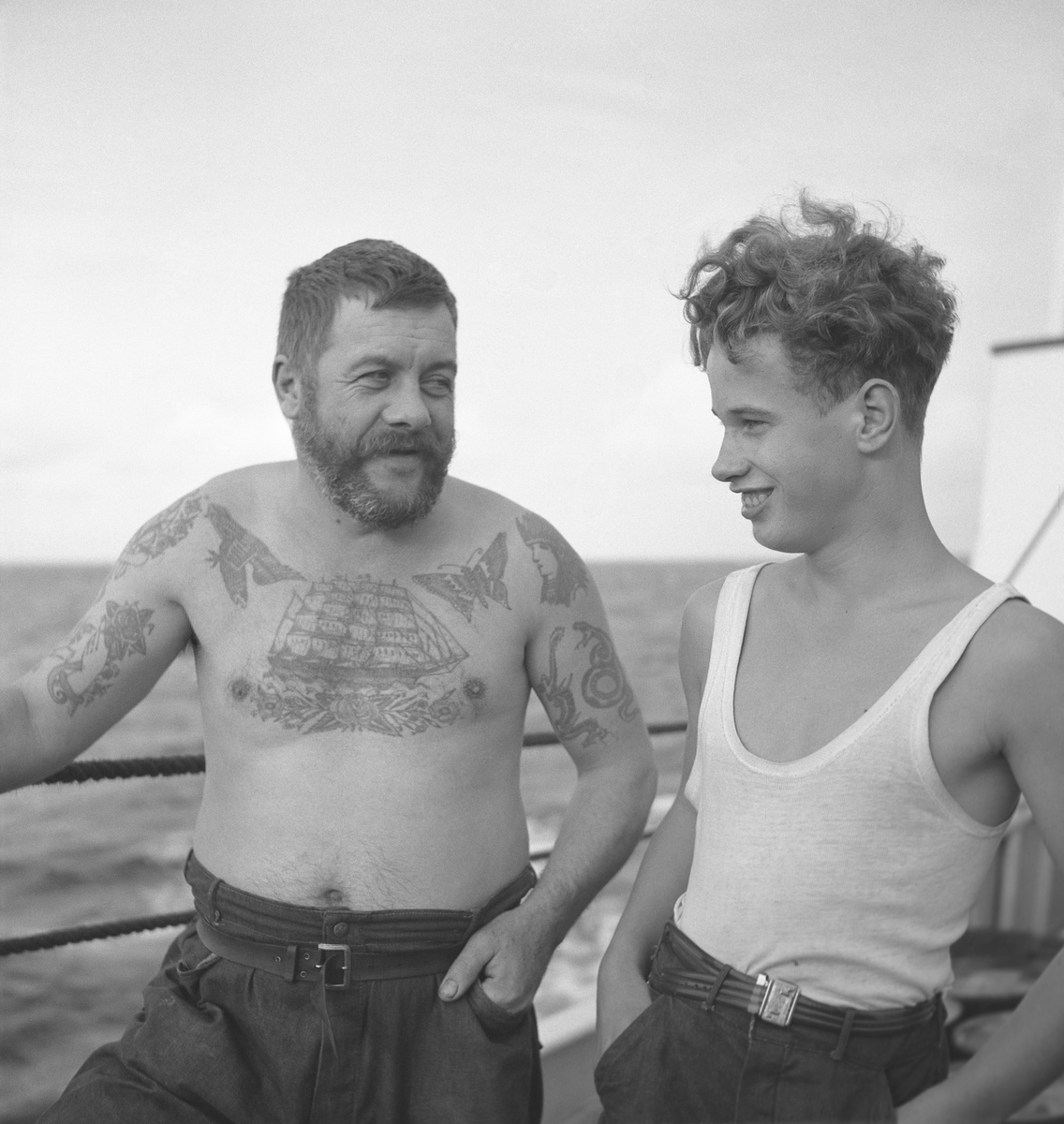Två män ombord på ett fartyg. En äldre man med tatueringar samt en yngre man.