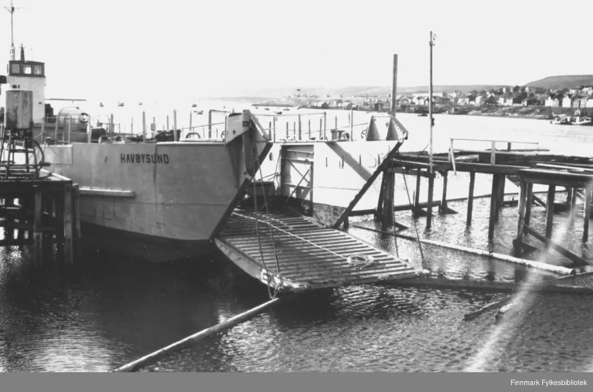 Båten 'Havøysund' ble brukt som lastebåt for å frakte materialer til gjenreisningen av Vadsø etter andre verdenskrig. På dette bildet ligger båten fortøyd ved kaia, med lasteplanet nede. I bakgrunnen ser man deler av Vadsø sentrum