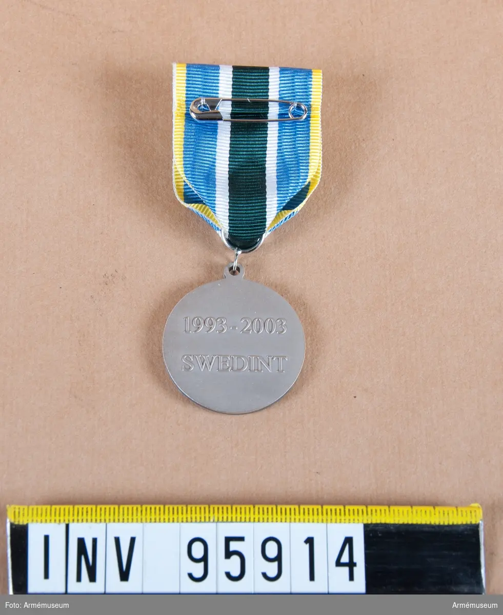 Försvarsmaktens internationella centrums minnesmedalj i silver, 8:e storleken.
Band: blått med gula kanter och en bred grön rand på mitten åtföljd på vardera sidan av en vit rand.
Medalj, släpspänne och band i blå ask klädd med blå sammet och vit siden.