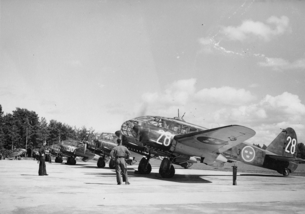 Sju stycken flygplan S 16 Caproni på flygfält på F 3 Malmen. Flygplansmekaniker omkring flygplanen. Fyra av flygplanen märkta med nummer 28, 30, 23, 27.