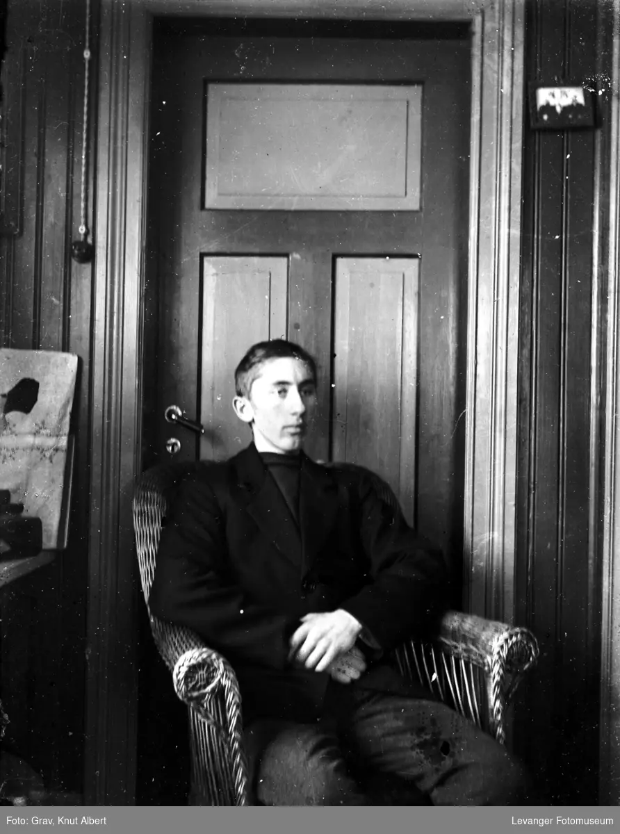 Portrett av en ung mann i en kurvstol foran en dør.