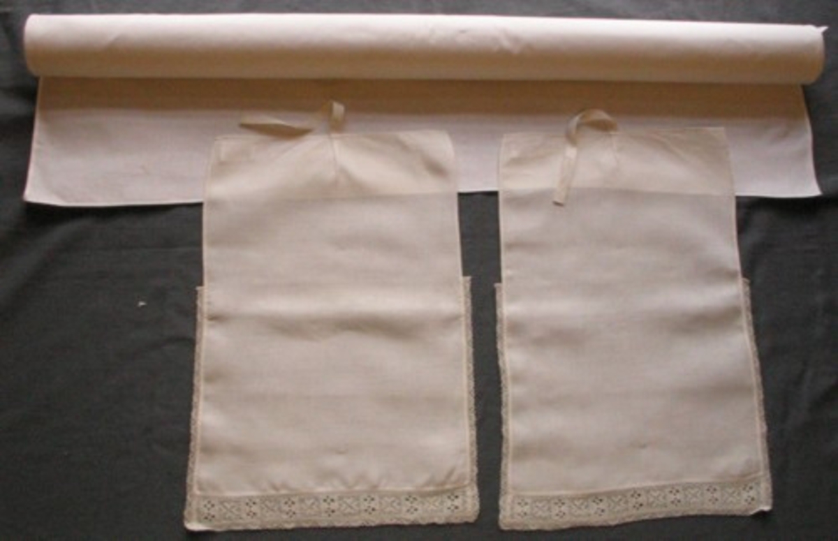 Klut i bomullstyg med klutband i linnetyg. Klutduken är ett slätt, fyrkantigt stycke, odekorerad och med smala, maskinsydda fållar runt om. Klutbanden är 390 X 278 mm med ett veck mitt på ena kortsidan där ett bomullsband (175 mm) är fastsytt. Handfållade. Nertill en 30 mm bred skånsk knypplad spets, klutbandet är dessutom till stora delar kantade med en smal skånsk spets; "Trehålstagg".