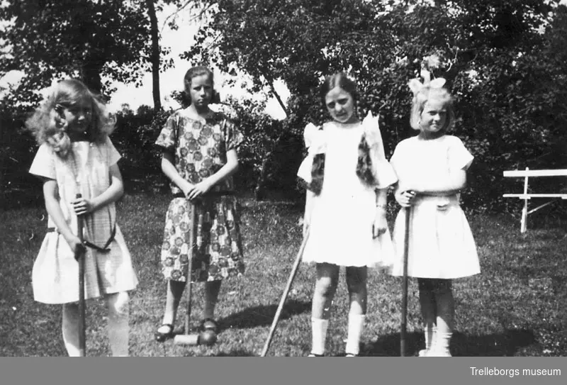 Fyra flickor spelar krocket i trädgården.