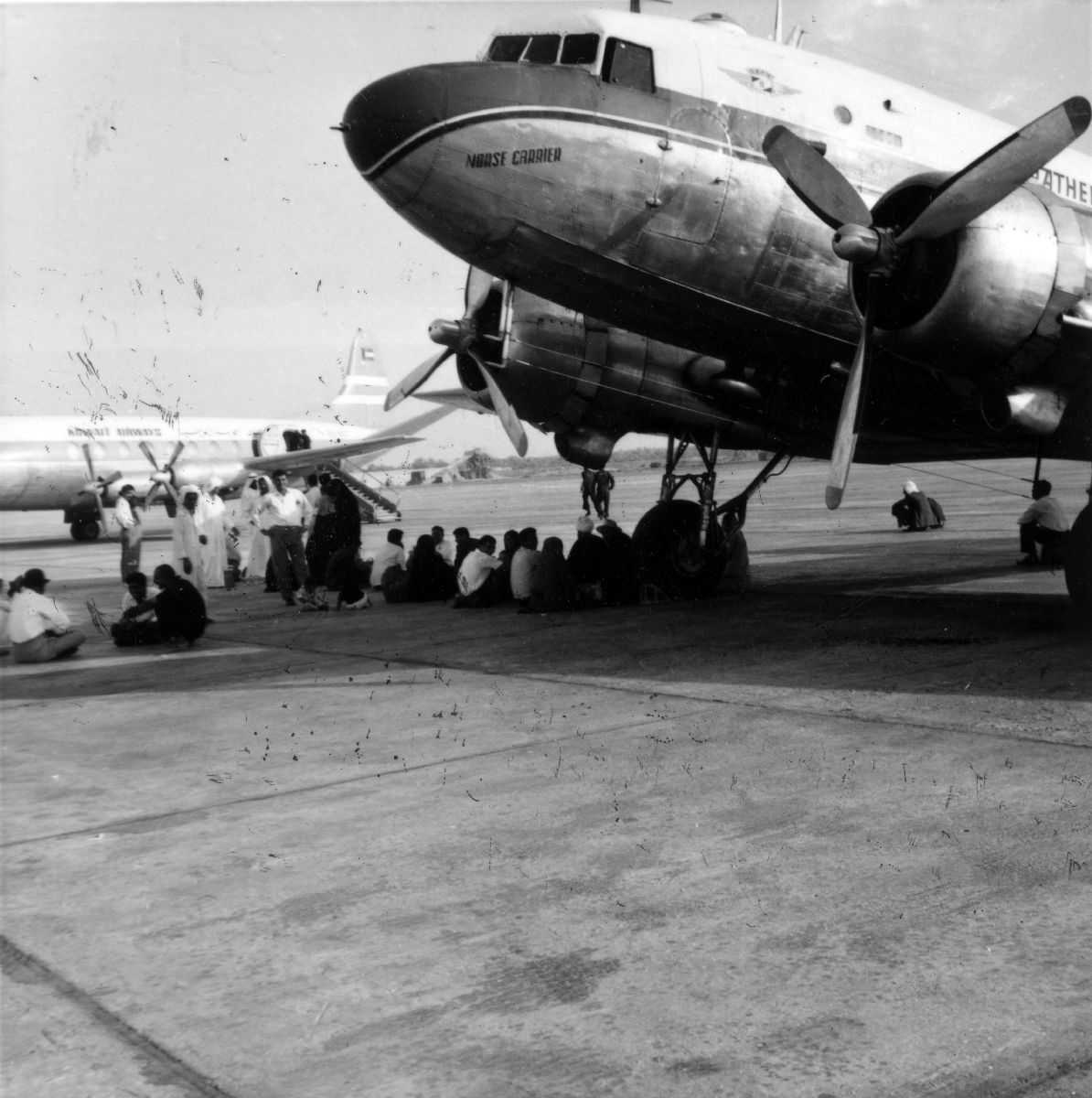 Lufthavn. Ett fly på bakken, DC-3 Dakota LN-PAS fra Braathens SAFE. Flere personer ved flyet. Et fly i bakgrunnen.