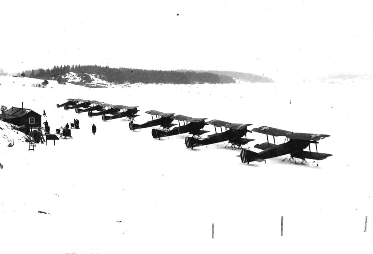 Flere fly oppstilt på bakken, Kaje og en FF.7 Hauk.  Flere personer og en bygning til venstre. Snø.