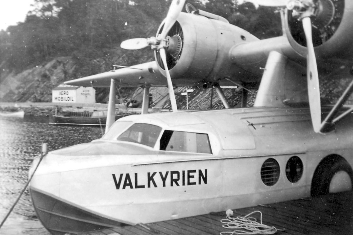 Sjøflyhavn, ett fly i vannkanten, Sikorsky S43 "Valkyrien", LN-DAG. Ligger ved flytebrygge/kai. Bygning med påskrift "AERO MOBILOIL" i bakgrunnen.