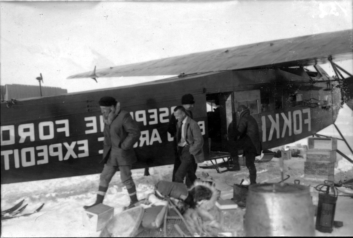 Fire personer, ved fly, Fokker FVII "Josephine Ford". Noe utstyr på bakken. Snø