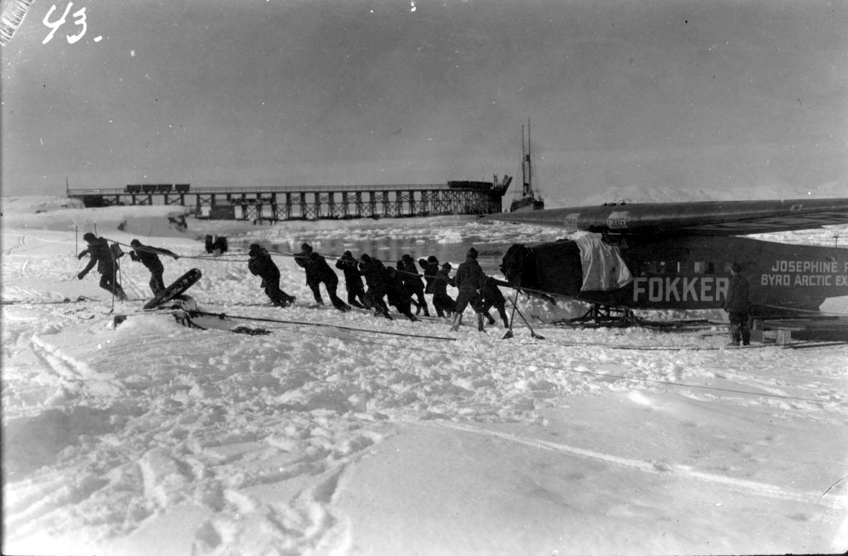 Flere personer trekker et fly på snø. Fokker FVII "Josephine Ford". 