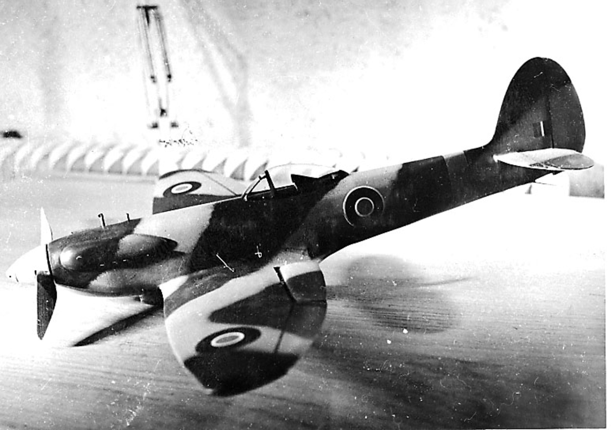 Fra album. 1 foto av modellfly, spitfire3, oppstilt på en benk.