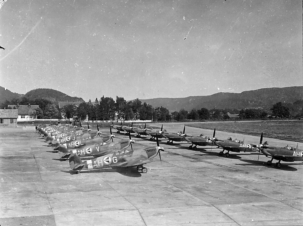 Lufthavn, 17 fly på bakken, Spitfire MK. IV, AH- fra 332 skv.  Flere bygninger i bakgrunnen.