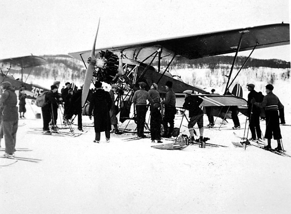 Flere personer - de fleste med ski - studeret et fly, Fokker CVD med skiunderstell, som står på bakken