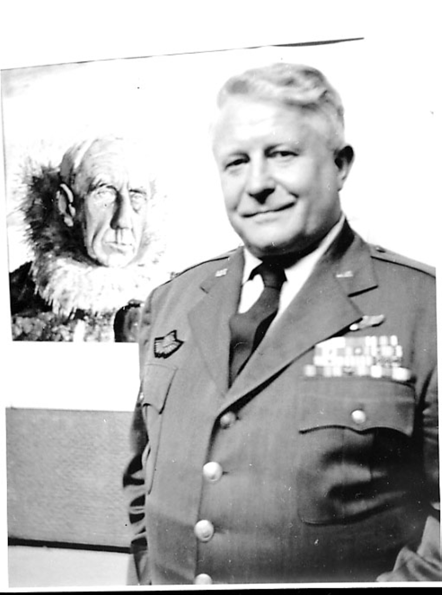 Portrett av person, mann i militæruniform foran et foto. Tatt innendøras av Roald Amundsen.