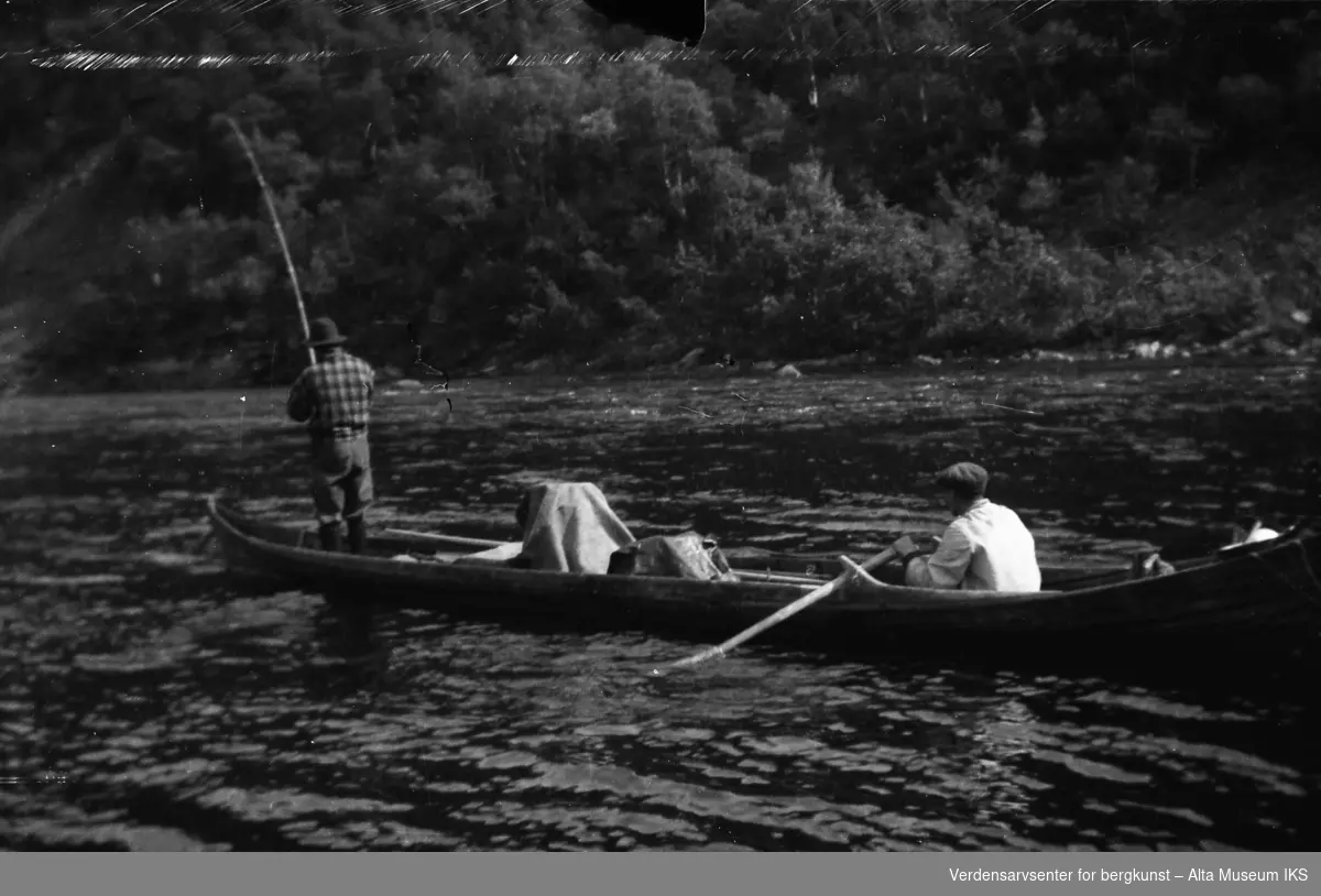 To menn i en elvebåt, den ene fisker og den andre ror.
Bildet er tatt i fiskesesongen på sommeren i 1949.