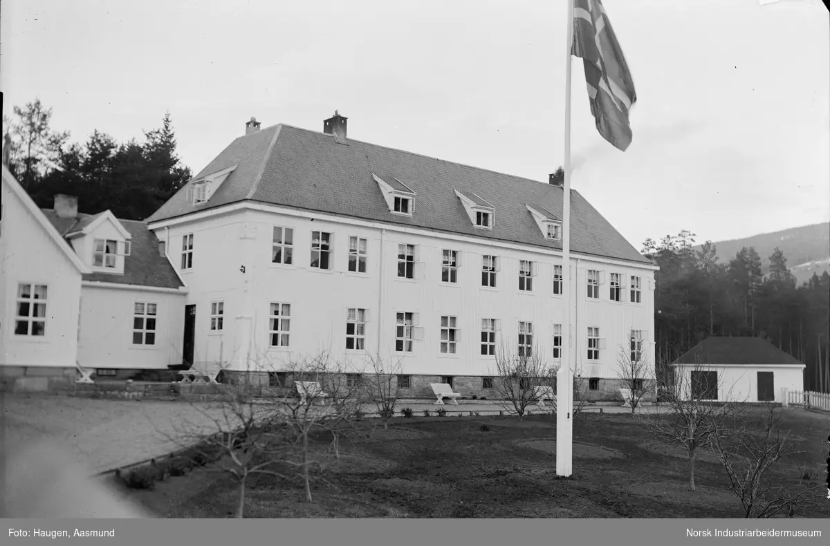 Tinn Helseheim med park og krakker på utsiden. Åpne vinduer i bygget. Flaggstang med norsk flagg.