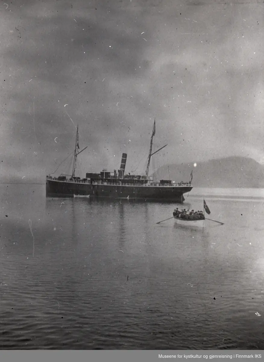 Fra 'Norske Lægers Nordkap og Varangerferd 1905'. D/S Hera for anker en eller annen plass langs kysten. Passasjerene ros med småbåter på land.