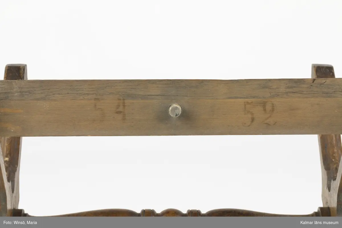 KLM 45337:1-2. Riksdagsstol. Består av en pulpet och en taburett. Pulpet (:1) av lackat trä med detaljer av metall. På pulpetens ena sida ett sluttande skrivbord med lock och lås. I högra hörnet hål och lock för bläckbehållare. Inuti bänken sekundärt skrivet med blyerts: C.A.A. * 18 9/8 46 (?). Nedan bänken ett tvärgående fotstöd. På pulpetens andra sida ett fastskruvat ryggstöd samt två armstöd. Dessa är stoppade med tagel och klädda med ett vinrött bomullstyg. På ena armstödet saknas tyget och ett vitt undertyg är synligt. Armstödens främre del är klädda i brunt läder. Ryggstödet kan lossas med en skruv och bakom, på pulpeten, siffrorna 67 i svart färg. Med blyerts även skrivet: Pettersson. På ryggstödets baksida, på sargen, möbelsnickarens stämpel, ett N inom en taggig oval ring. Även 166 i svart färg. Hela möbeln har svarvade raka, rektangulära ben och tvärgående fötter. Överstycke med svarvade knoppar och utsparade detaljer. På överstyckets mitt en mässingsplåt med instansade siffror: 77. Till pulpeten hör en taburett (:2) som, när det placeras intill ryggstödet, blir en stol. Taburetten är av lackat trä med svarvade kryssben och mittslå. Under två av benen små trähjul. Stoppad löstagbar sits klädd med likadant vinrött tyg som på pulpetens ryggstöd. Sitsen går att lossa och på dess undersida är möbelsnickarens signatur stämplad i träet: F. RAMBACH. Även 67 i svart färg. På sargen är det också siffror och bokstäver skrivet med blyerts: 97, IK eller IJG. På taburettens sarg spår efter stämplar: 54, 52.