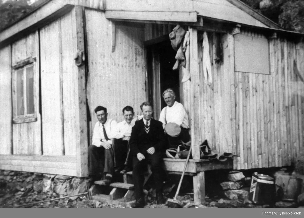 Portrettfotografi av en gruppe som sitter på trappa til en brakke. Fra venstre: Odin Emaus, Odin Nilsen, Agnar Iversen og Håkon Rapp.