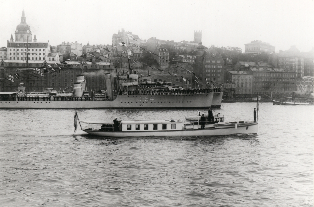 Motorslupen Eugen med konung Gustav V ombord passerar brittiska jagarna Vansittart (D64) samt Mackay vid Stadsgårdskajen i Stockholm, sept 1922. Jagarna[s besättning] mannar reling och hälsar den kungliga slupen.