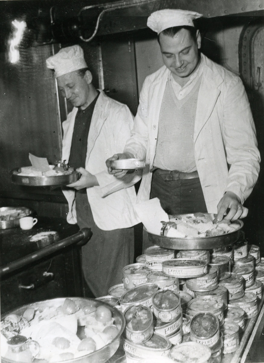 Två män i köket lägger upp mat på brickor.