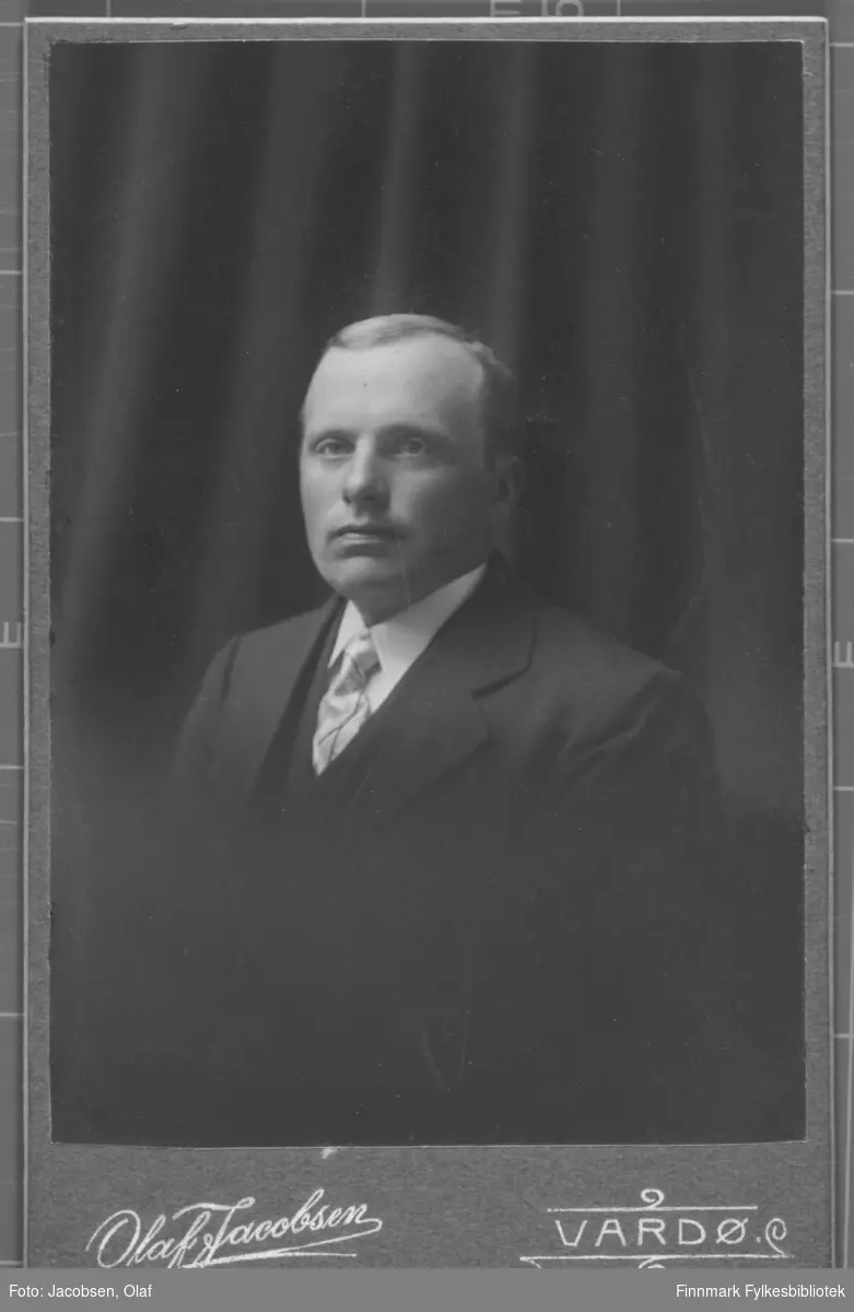 Portrett av en mann kledd i en mørk dress vest slips og hvit skjorte. I studio ateliere, mørk gardin som bakgrunn.  Albumet med bildet kommer fra Ekkerøy, kanskje han kommer derfra.
